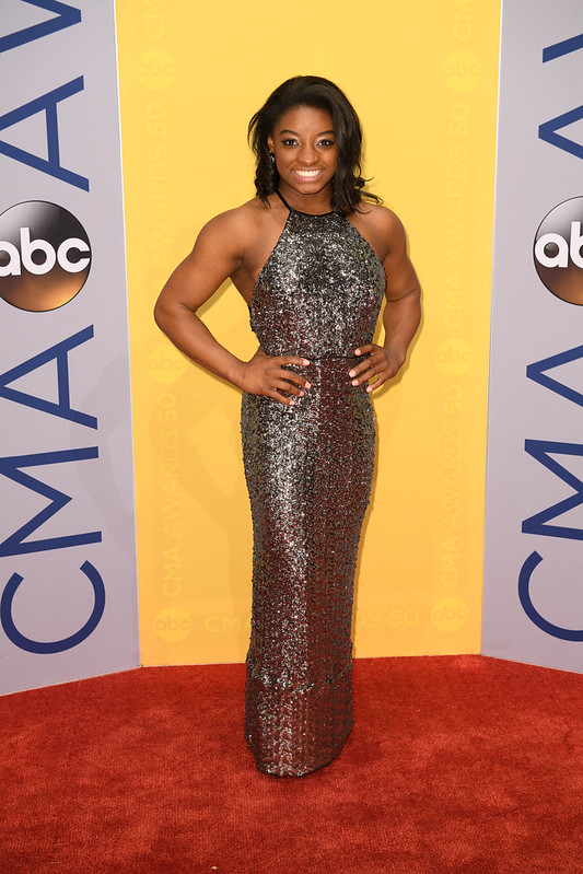 Simone Biles with her hands on her hips smiling at the camera at the CMA Awards